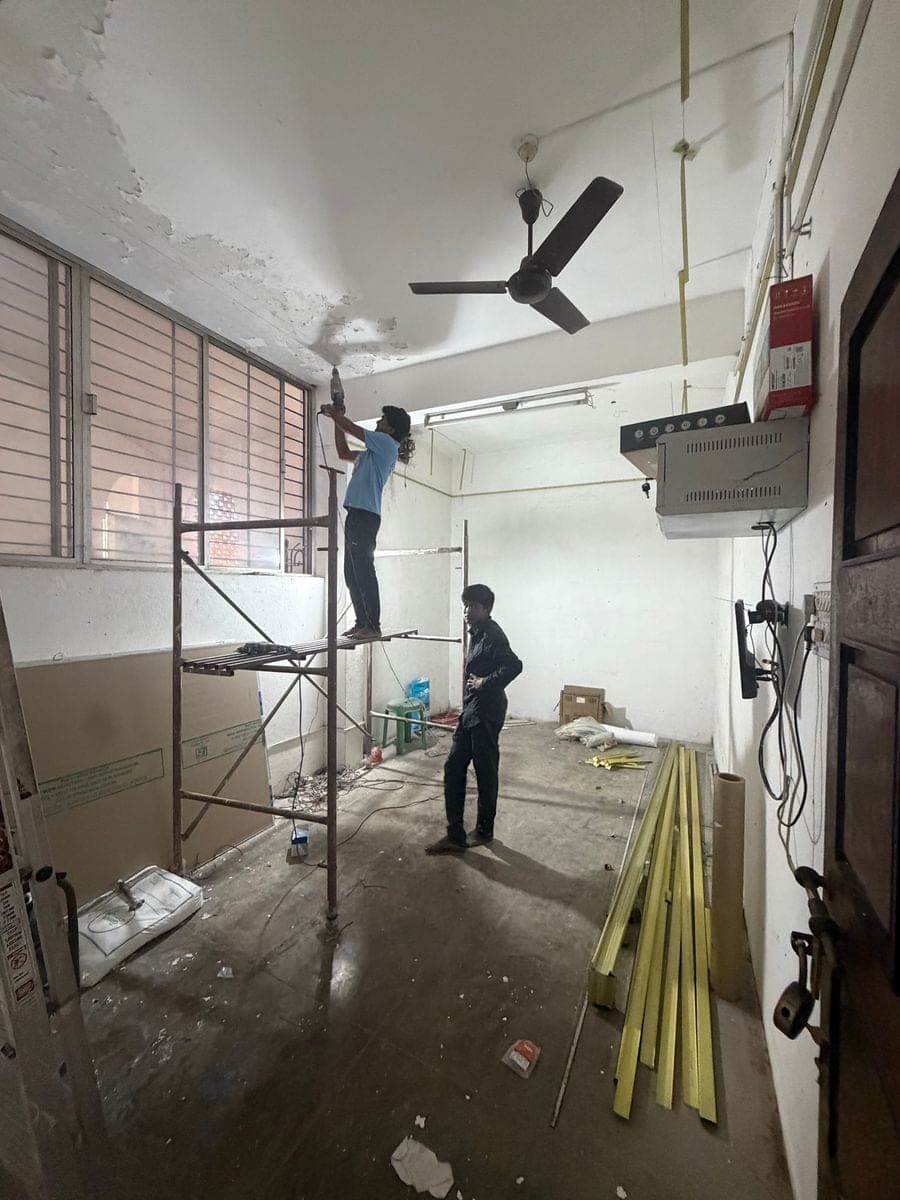 A worker on scaffolding drills into the old ceiling while ceiling channels lie on the floor